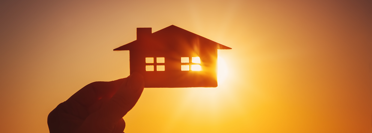 Hand houdt een huis vast met op de achtergrond een zonsondergang