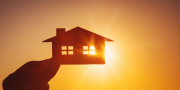 Hand houdt een huis vast met op de achtergrond een zonsondergang