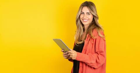 Blonde vrouw met tablet in de hand op een gele achtergrond